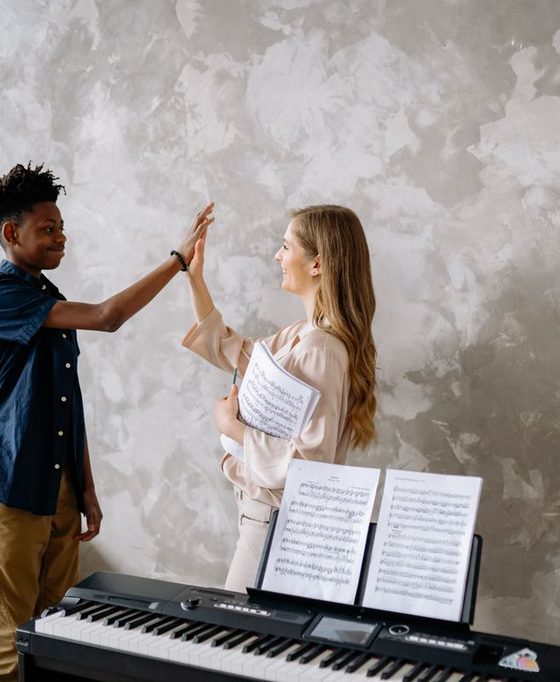 A music teacher and student sharing a high-five at the keyboard