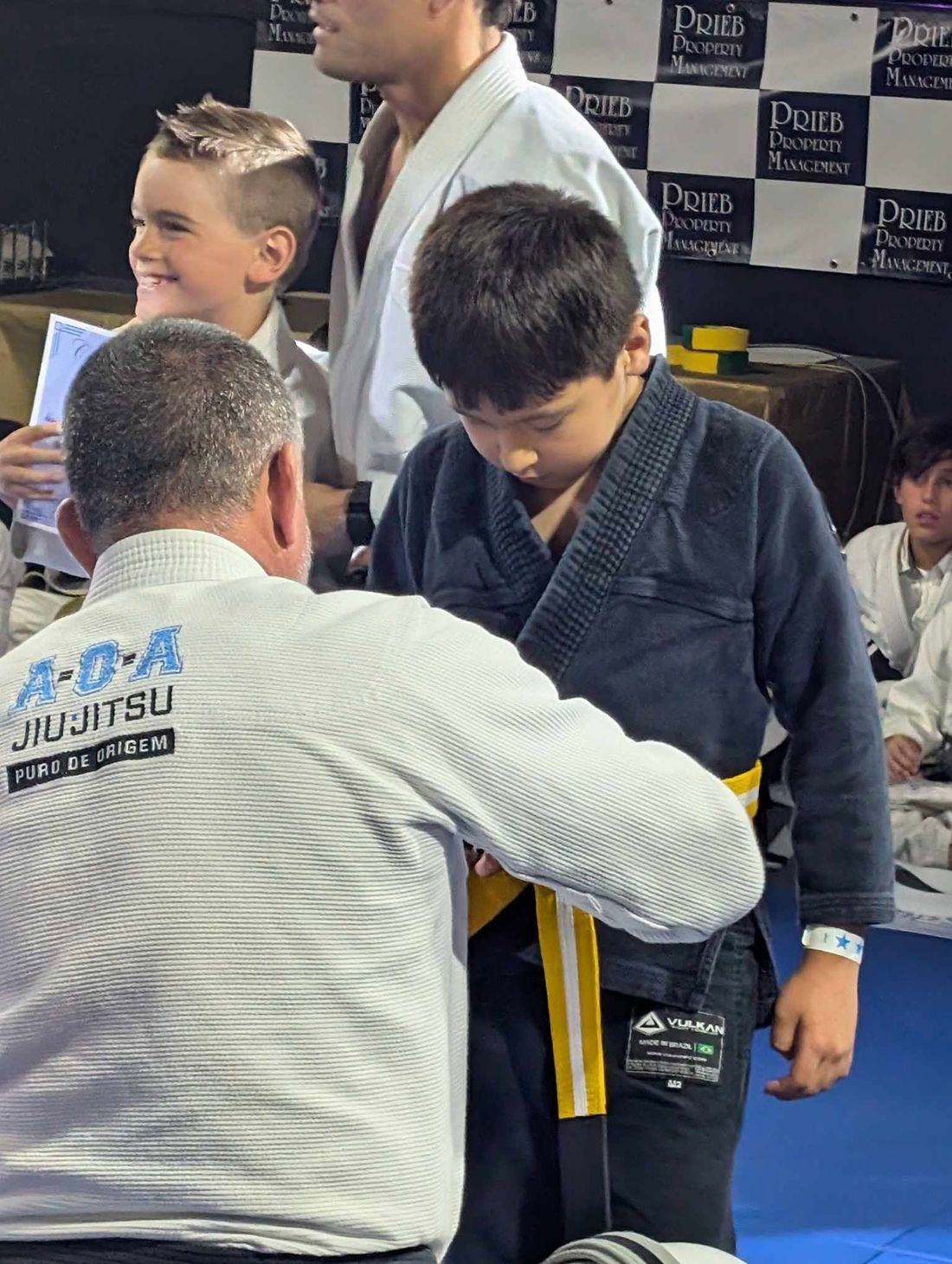 A young jiu-jitsu student having his new belt tied by his instructor at a studio.
