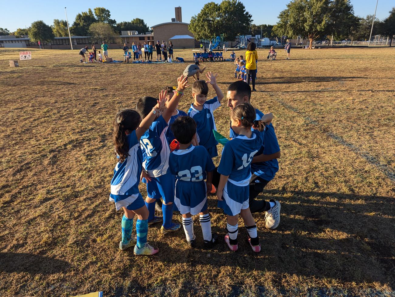 A youth soccer team huddled together with their coach, hands stacked in the center after a game.